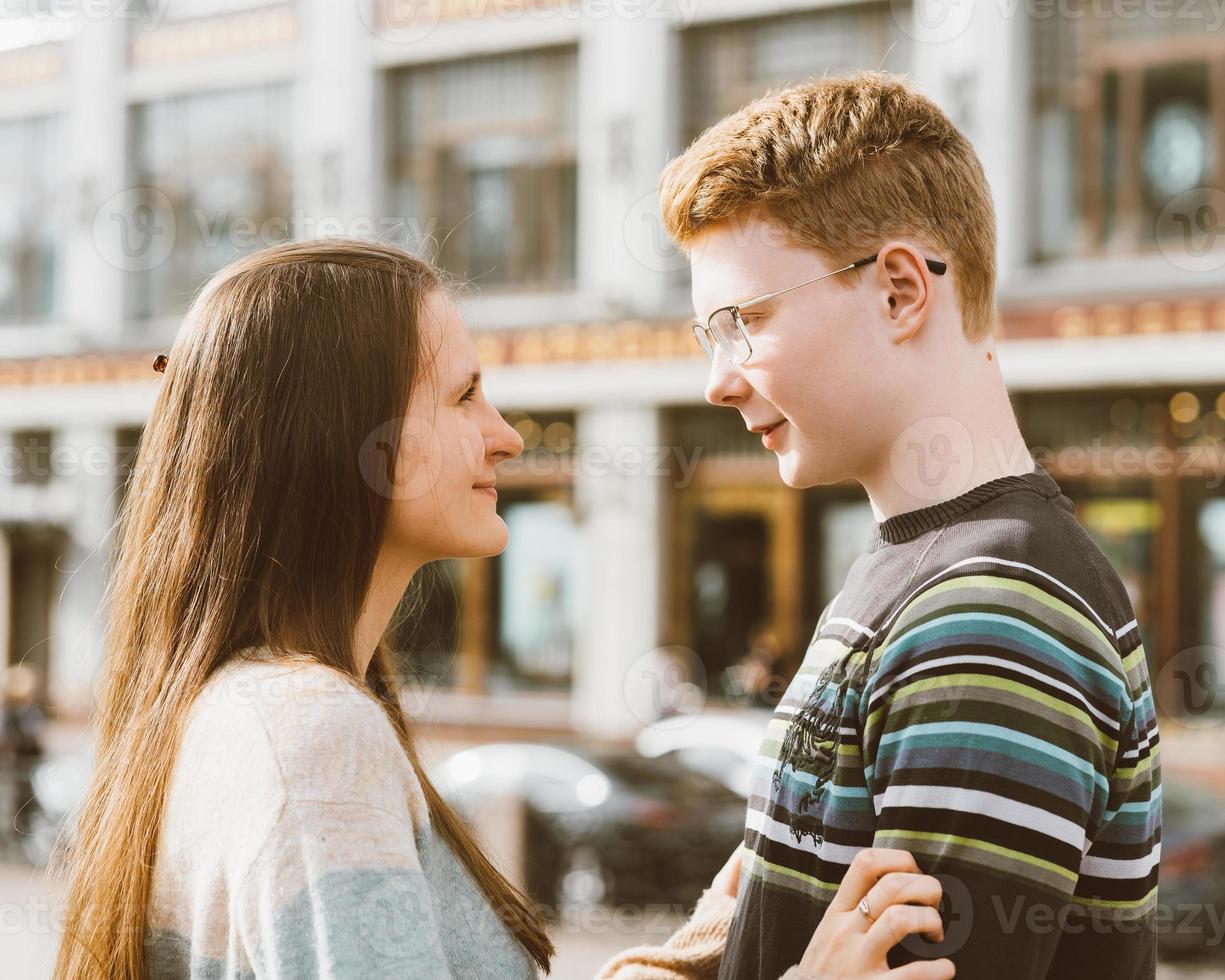Male and female person looking at each other, young couple full of love. The redhead boy looks tenderly at girl and kiss. Concept of teenage love and first kiss, love, relationship. City, waterfront. photo