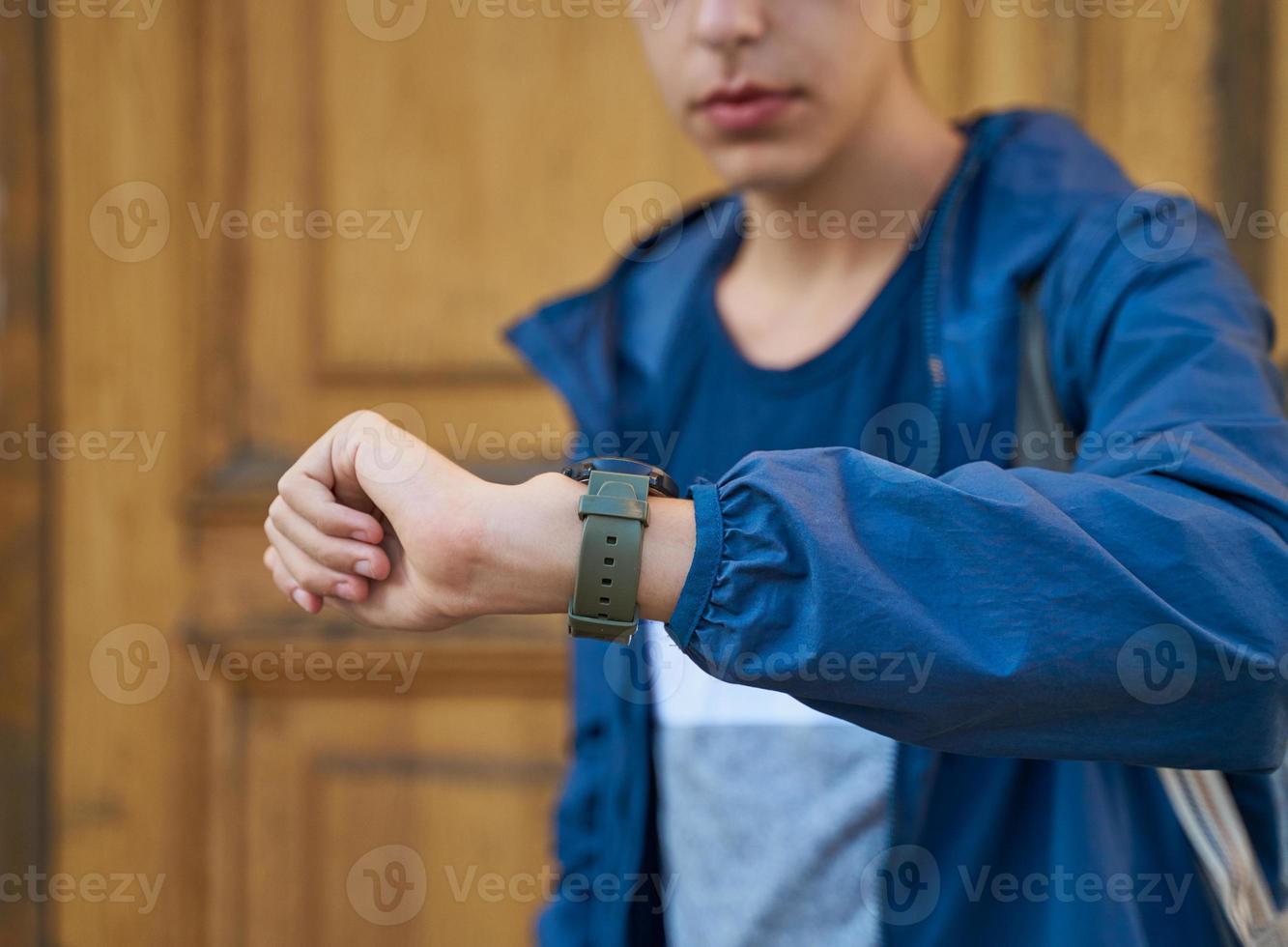adulto joven mira el reloj, esperando una reunión con amigos. un hombre está esperando a una mujer en una calle de la ciudad en una cita, mirando el reloj foto