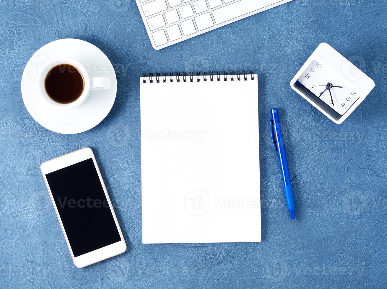 el bloc de notas abierto con una página blanca limpia, un bolígrafo y una taza de café sobre una mesa de piedra azul oscuro envejecida, vista superior foto