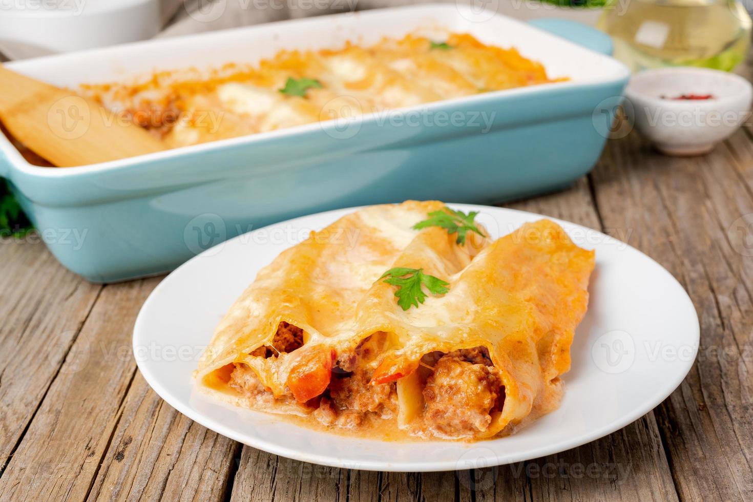 Cannelloni with filling of ground beef, tomatoes, baked with bechamel tomato sauce, side view, old dark wooden background photo