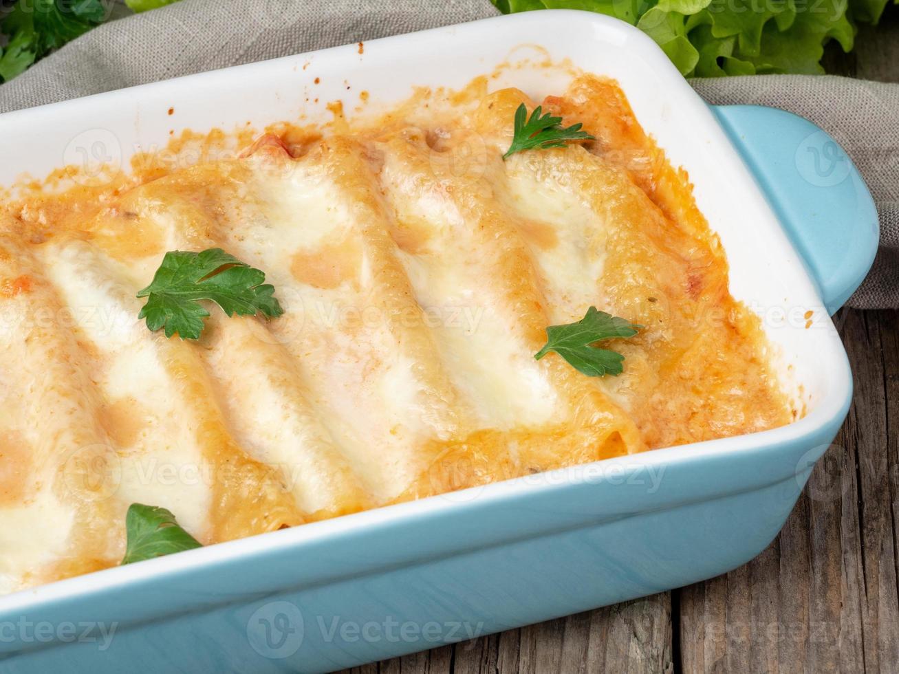 Cannelloni with filling of ground beef, tomatoes, baked with bechamel tomato sauce, side view, old dark wooden background photo