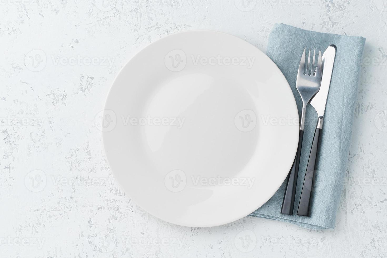 Limpie el plato blanco vacío, el tenedor y el cuchillo en la mesa de piedra blanca, copie el espacio, maqueta, vista superior. foto