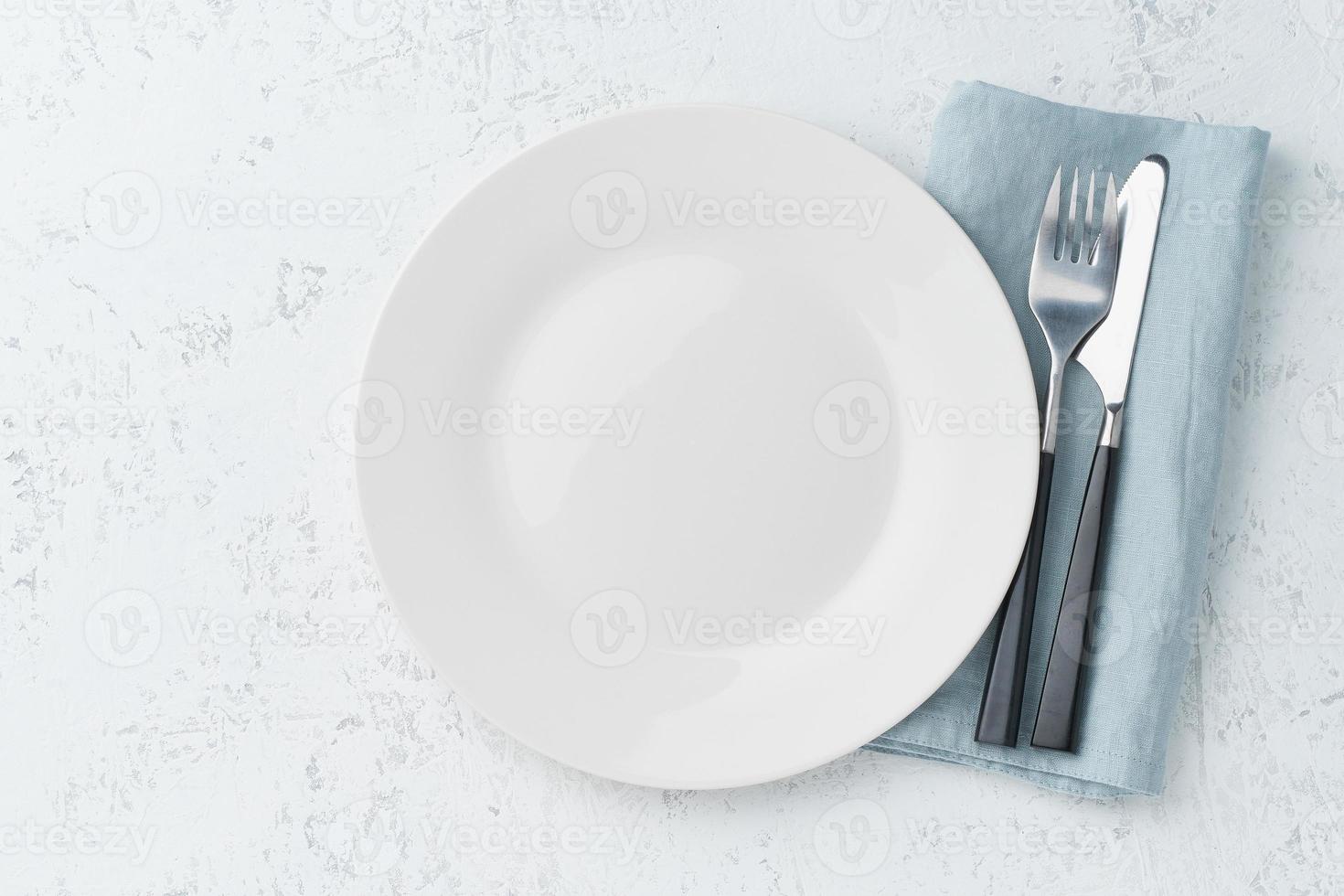 clean empty white plate, fork and knife on white stone table, copy space, mock up, top view. photo
