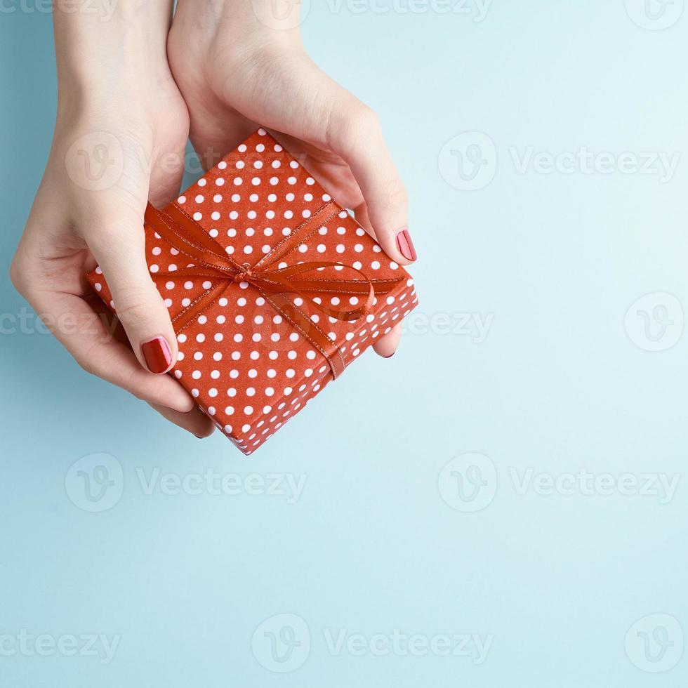 woman hands holding red gift with ribbon, manicured hands with nail polish photo