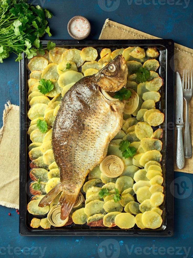 carpa al horno, pescado entero al horno con patatas en rodajas en una bandeja grande. plato tradicional polaco foto