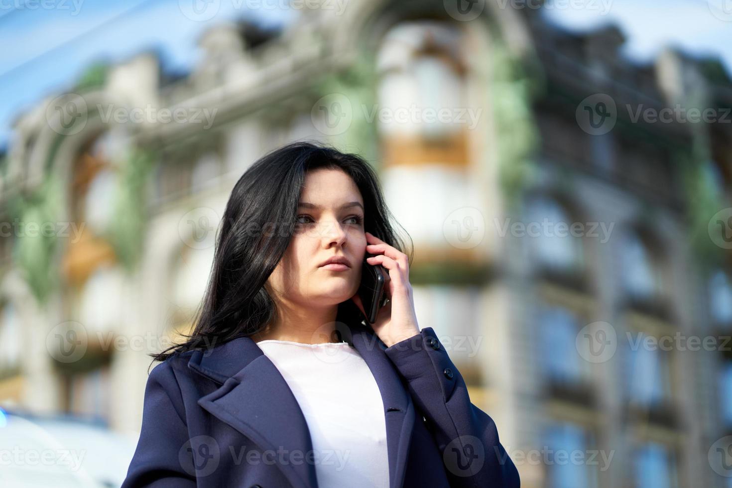 Woman with long hair talking on phone. Autumn or winter, girl in outdoor. Beautiful intelligent brunette in street of Saint-Petersburg in city center, copy space photo