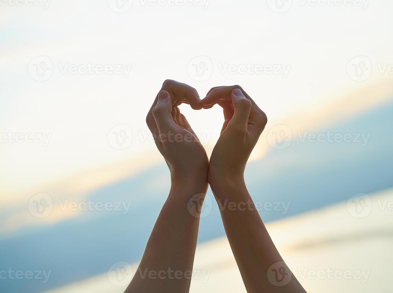 mano femenina y masculina que muestra el corazón, símbolo de amor, fondo de playa, puesta de sol vespertina foto