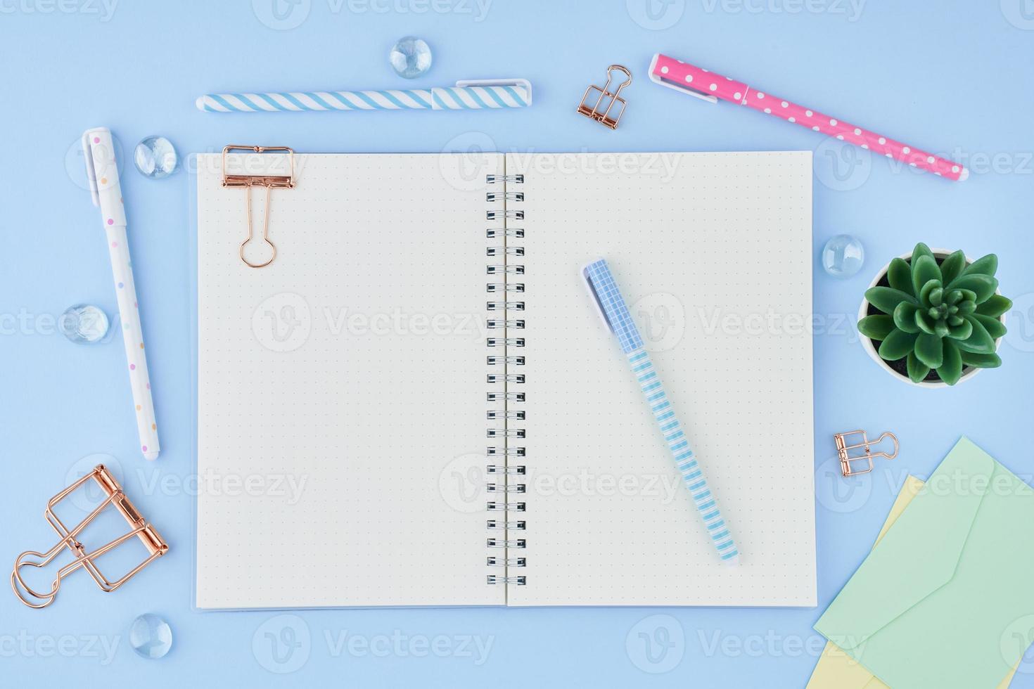 Blank notepad page in bullet journal on bright blue office desktop. Top view of modern table with notebook, stationery. Mock up, copy space, concept for diary photo