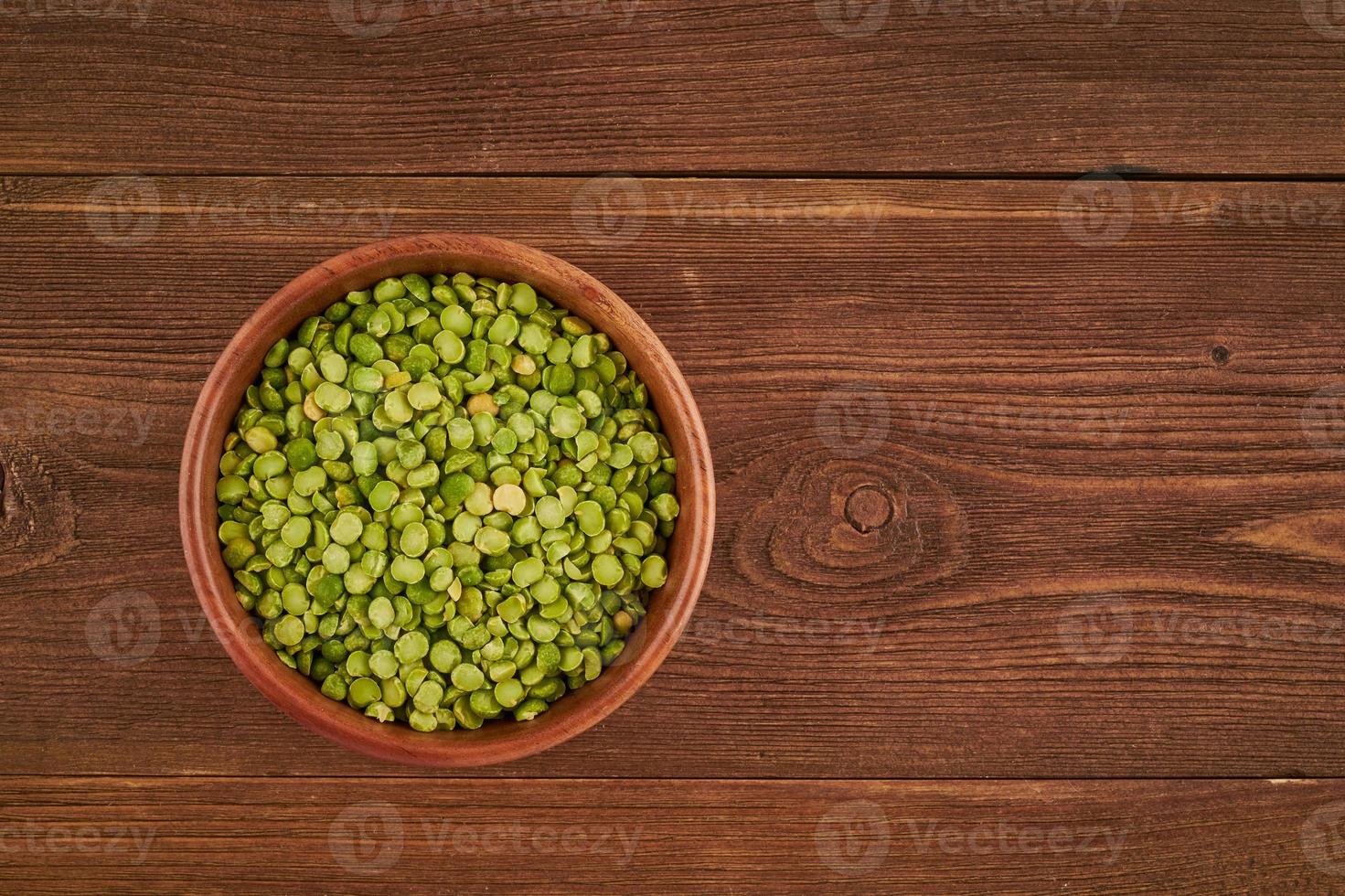 green peas in wooden bowl on brown background, top view, copy space photo