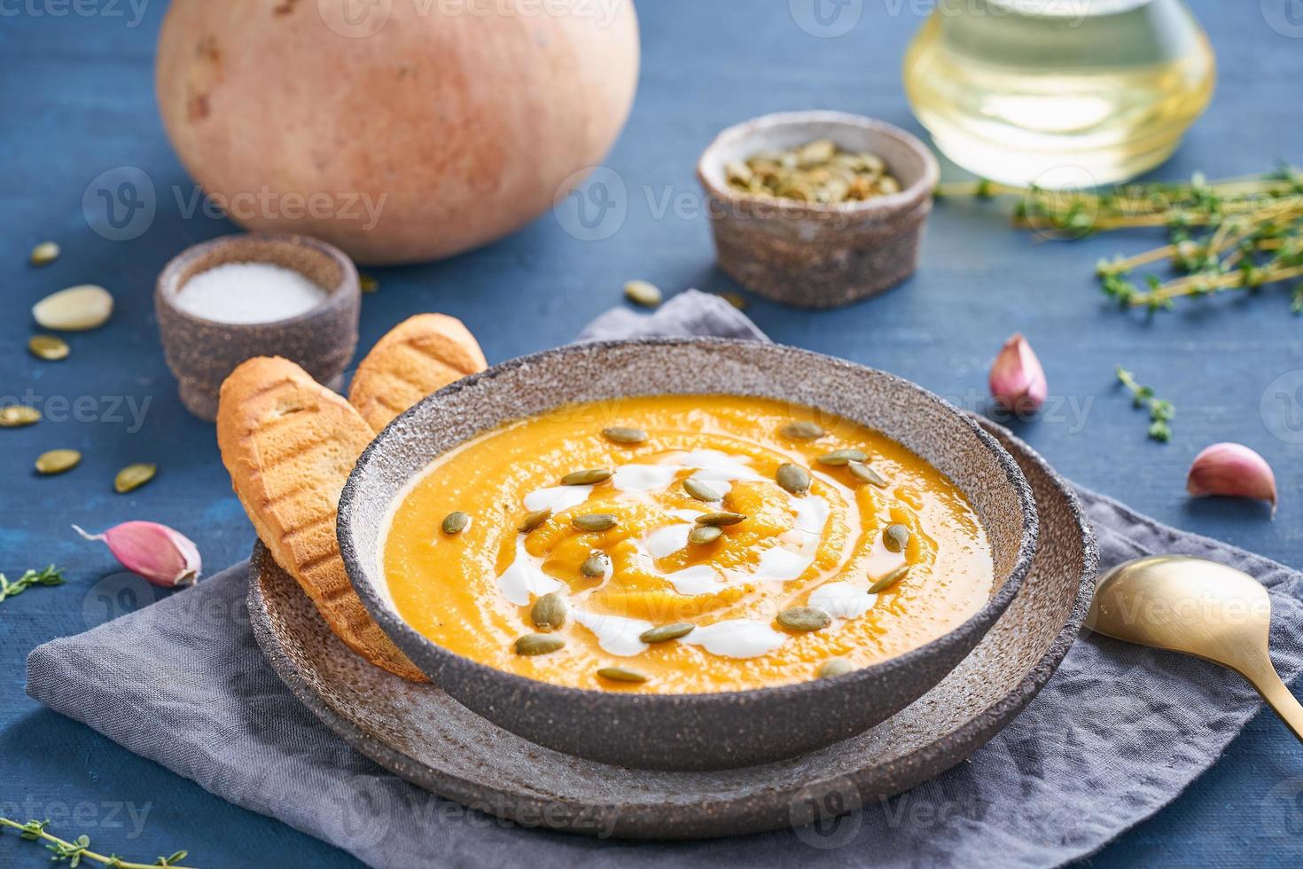 Pupmkin cream soup puree on dark bright blue wooden table, seeds, toast, dietary vegetarian lunch, side view. photo