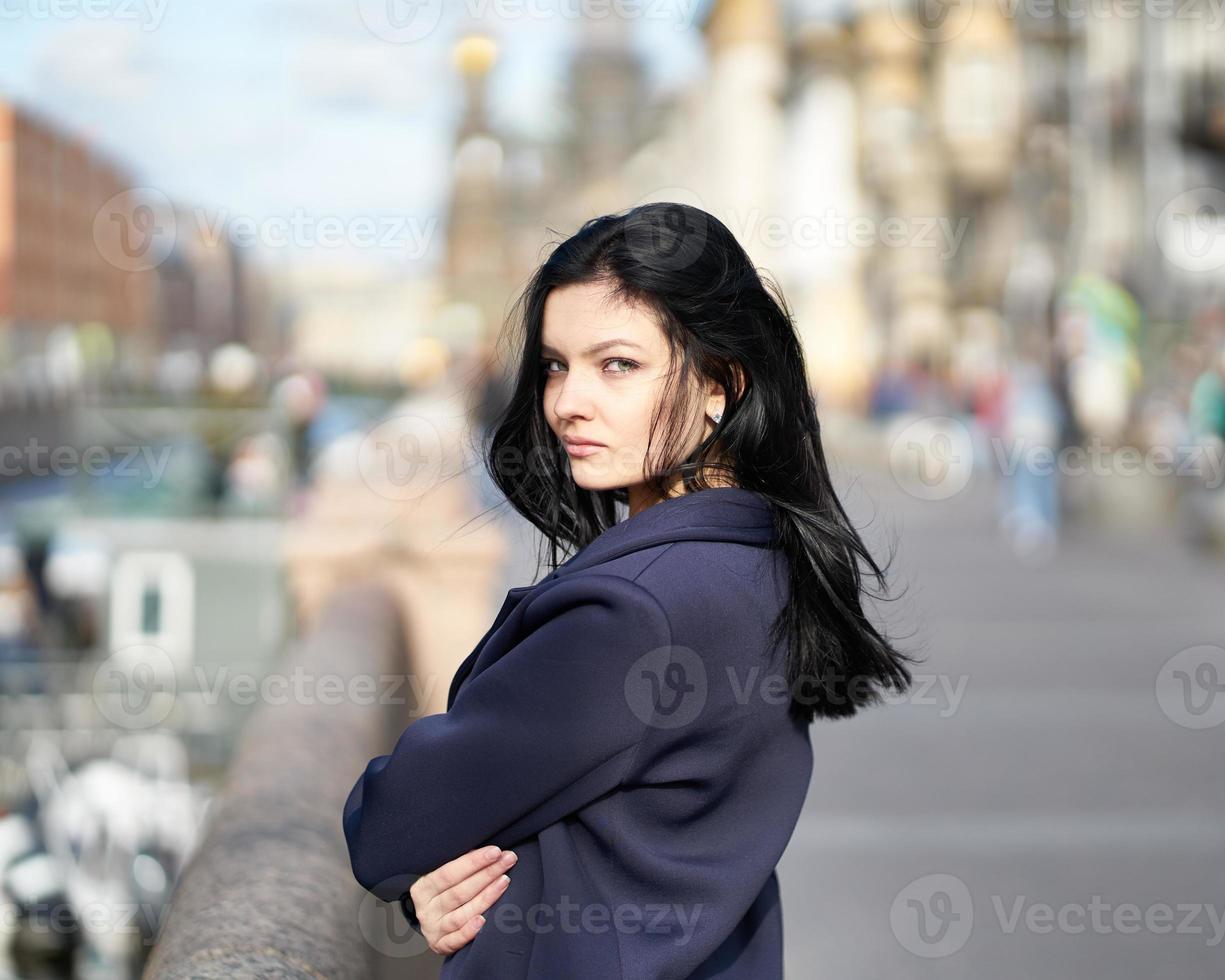 Portrait f beautiful intelligent brunette who walks down street of Saint-Petersburg in city center. Charming thoughtful woman with long dark hair wanders alone, immersed in thoughts photo