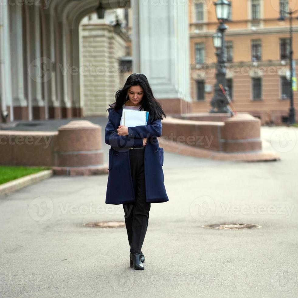 hermosa estudiante morena inteligente seria sosteniendo cuadernos y libros de texto, va caminando en la universidad en la calle de st. petersburgo una mujer encantadora con el pelo largo y oscuro está estudiando en el curso foto