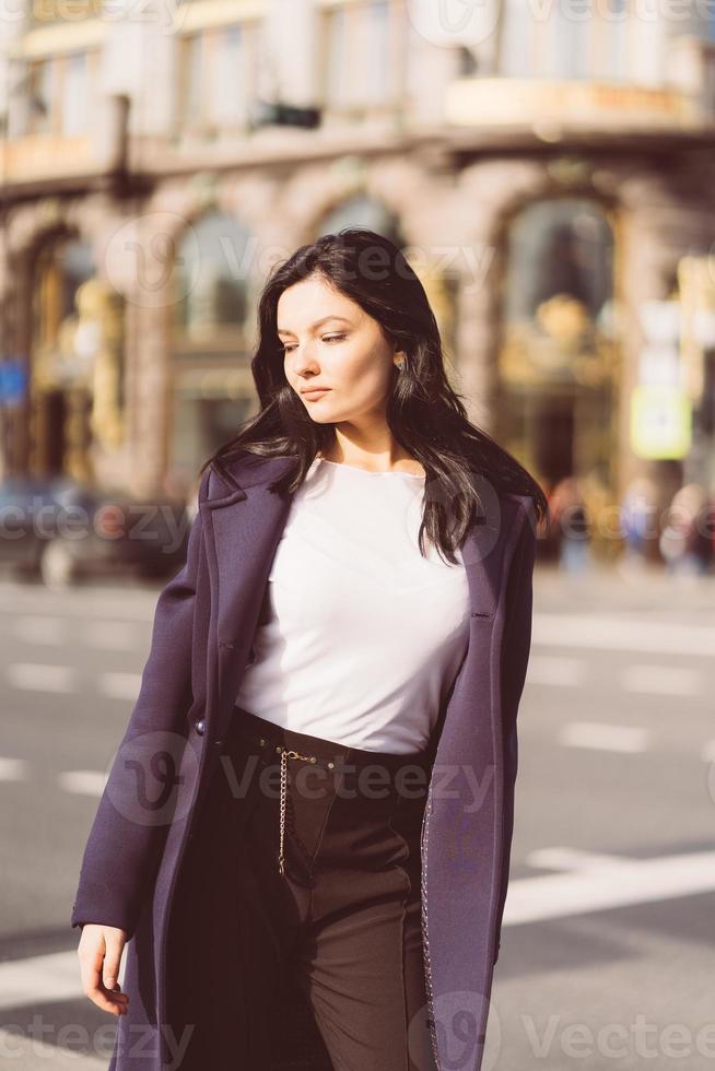 Portrait f beautiful intelligent brunette who walks down street of Saint-Petersburg in city center. Charming thoughtful woman with long dark hair wanders alone, immersed in thoughts photo