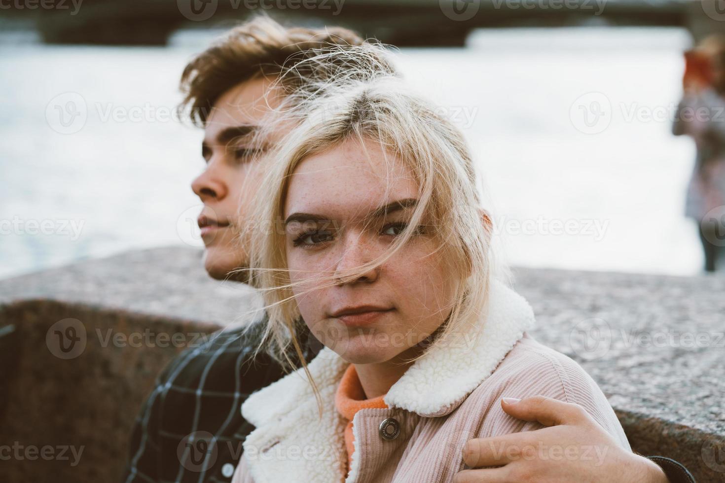 Teenagers in love sit on the waterfront in the city center, resting in autumn sun. Concept the first teenage love, the beginning of relations. A boy and a girl meet on date, couple. Girl close up photo