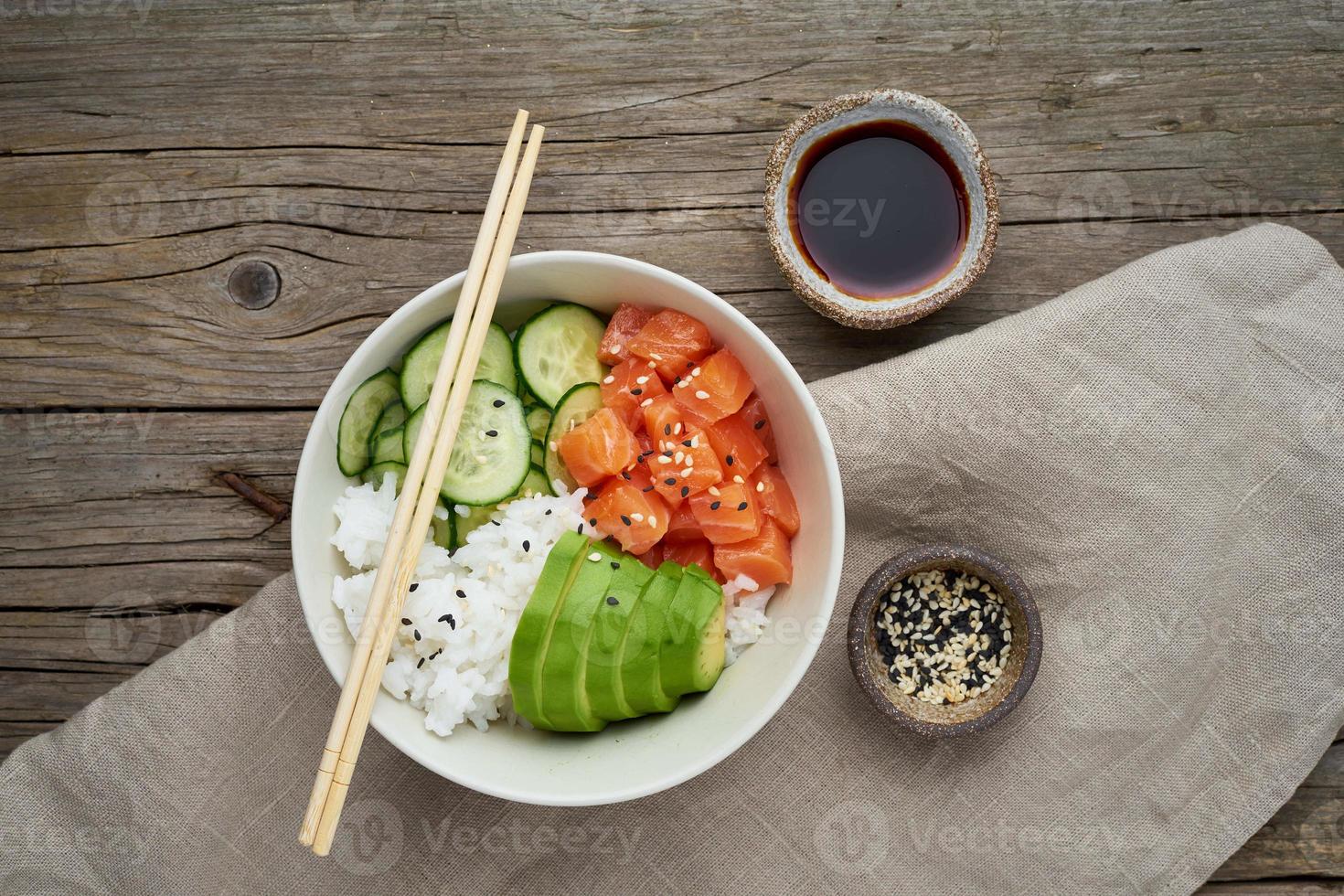 Poke bowl de salmón con pescado fresco, arroz, pepino, aguacate con sésamo blanco y negro. mesa de madera antigua. concepto de comida foto