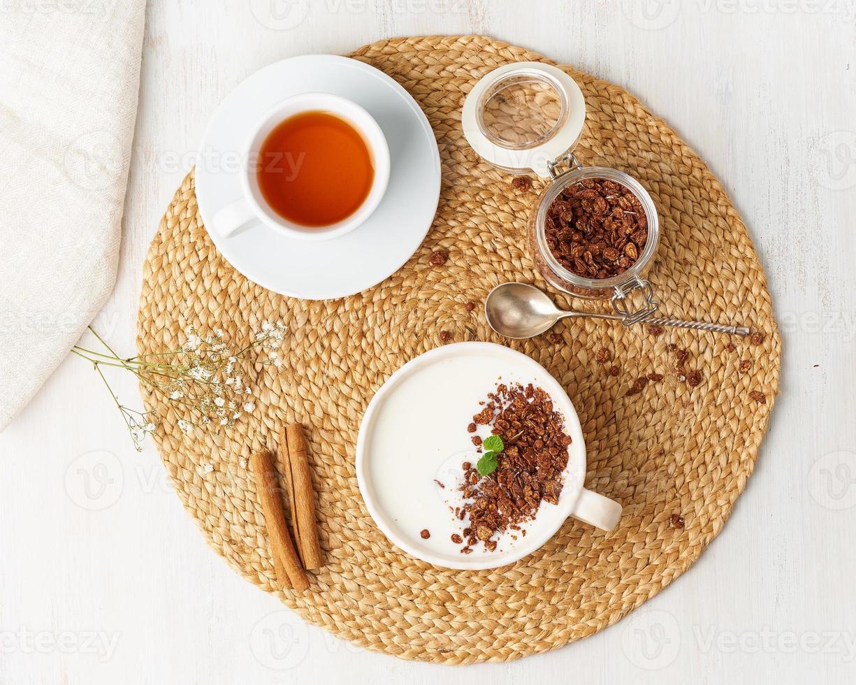 yogur con granola de chocolate en taza, desayuno con té sobre fondo beige, vista superior. foto