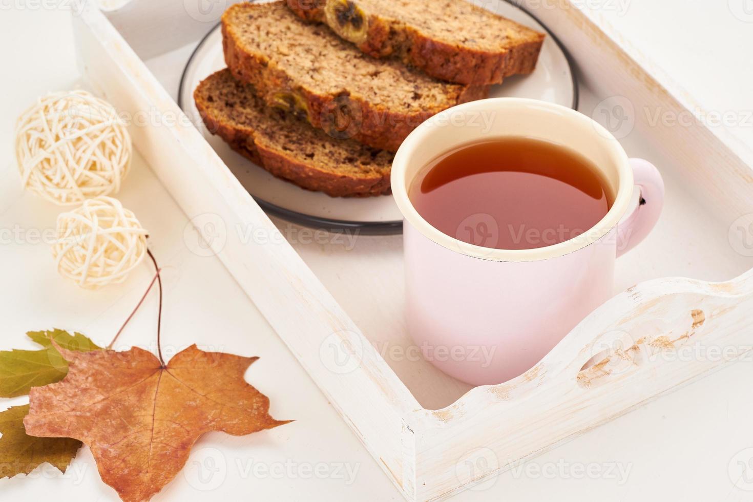 comida de otoño: rebanadas de pan de plátano, una taza de té, hojas secas, mesa de madera blanca. acogedor hogar de invierno. vista lateral, espacio de copia foto