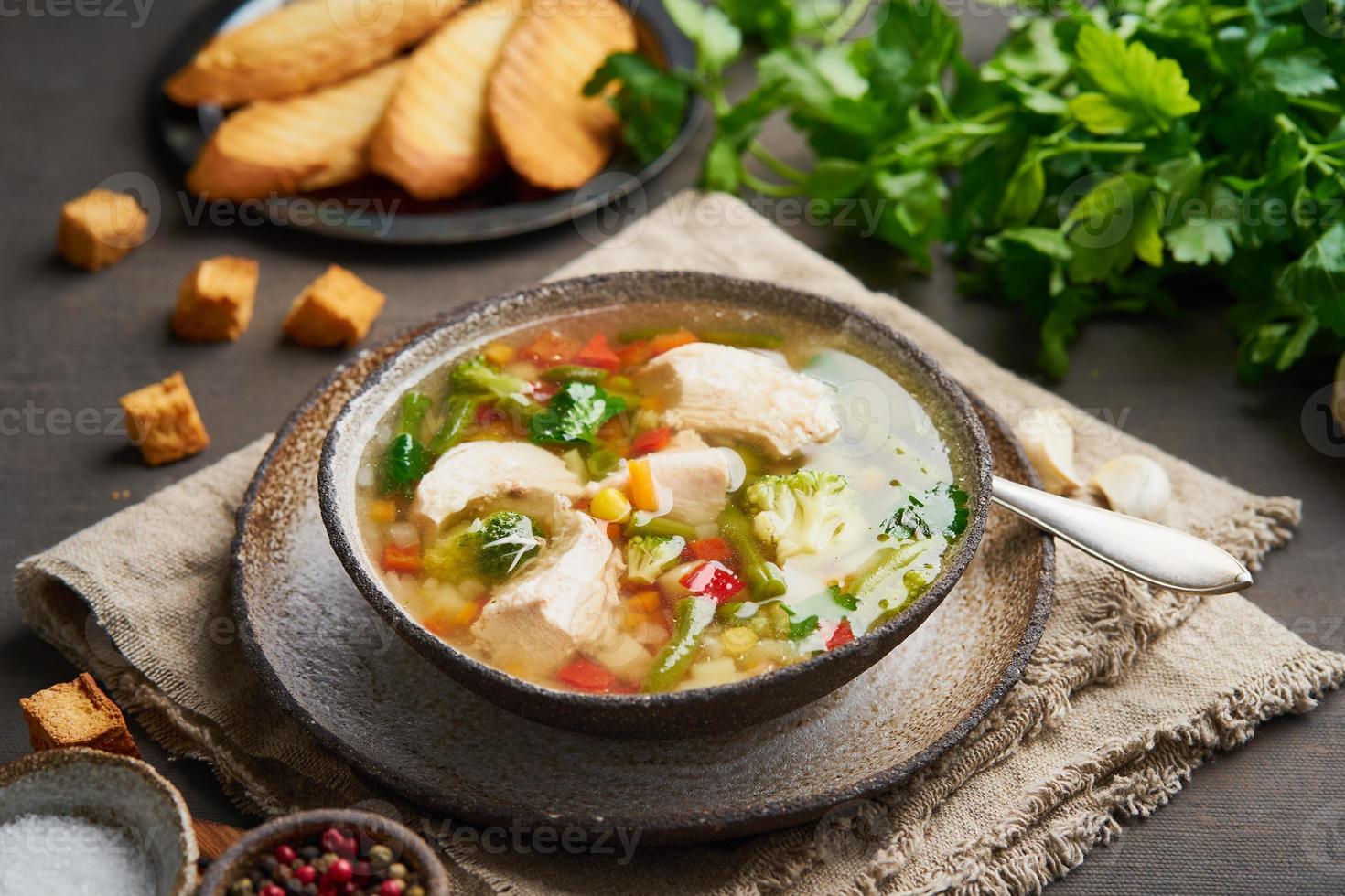 Homemade chicken soup with vegetables, crouton, broccoli on a dark brown background, side view photo