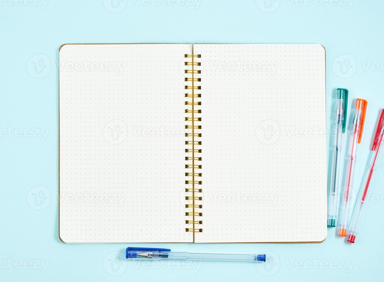 Blank notepad page in bullet journal on blue office desktop. Top view of modern bright table with notebook. Mock up, copy space photo
