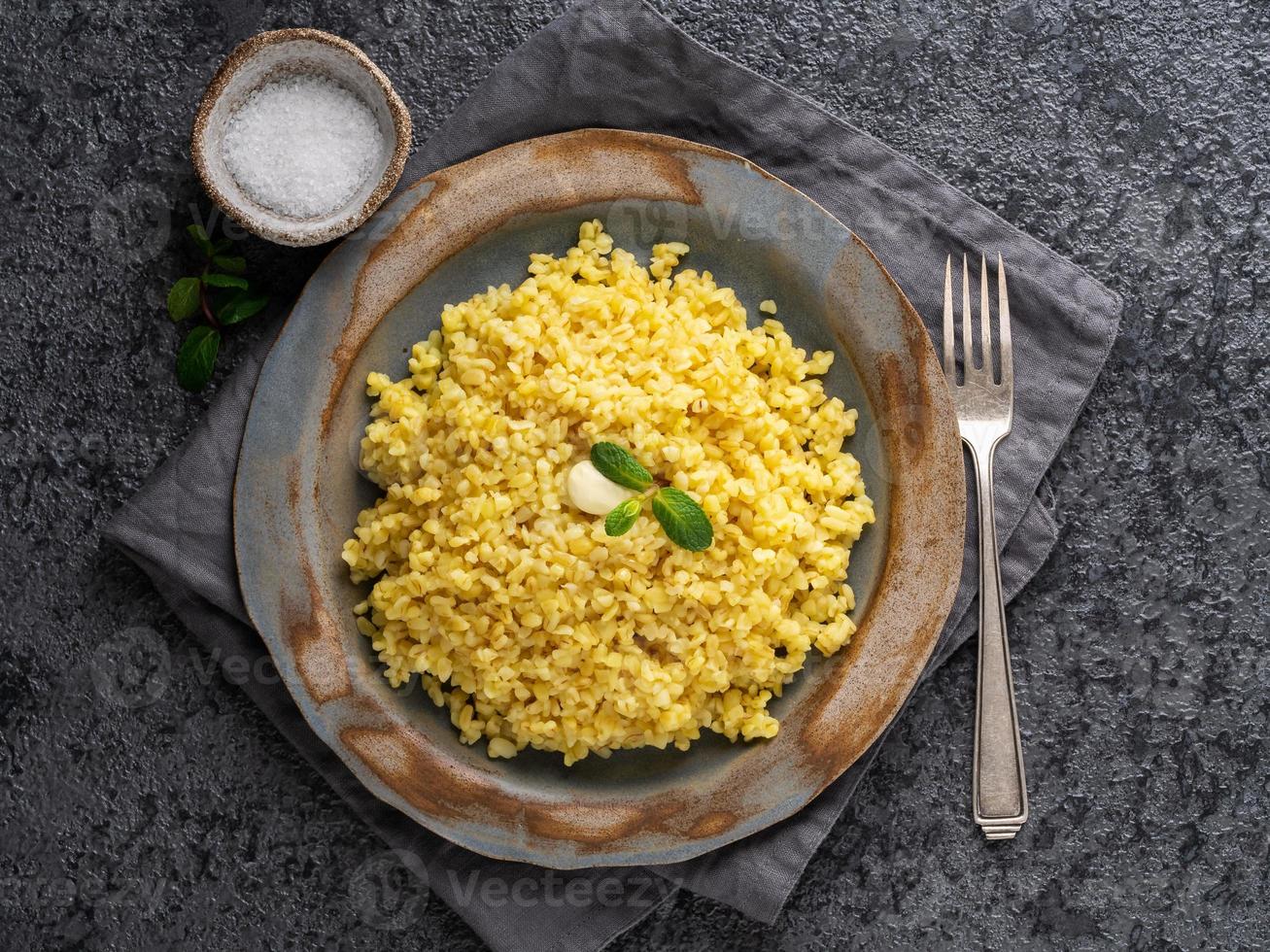 Bulgur wheat. Boiled bulghur cereal in plate on dark grey stone table. Healthy vegetarian food, top view photo