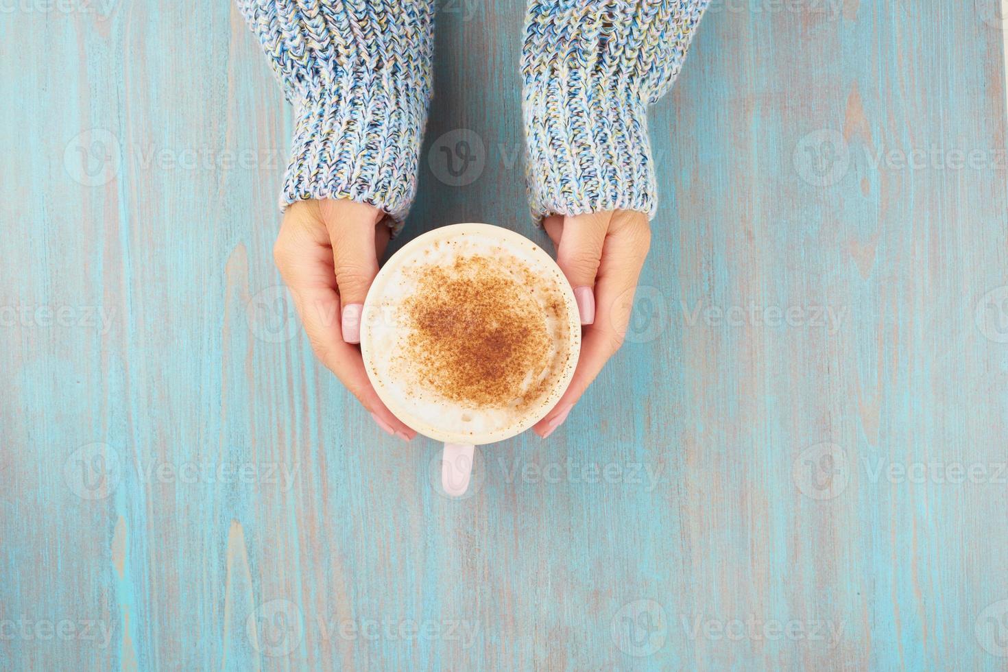 hands holding cup of hot chocolate, blue wooden table, blue cozy sweater, beautiful pink manicure, home style, autumn morning, close up, top view, copy space photo