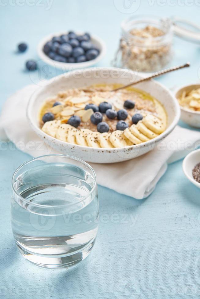 Oatmeal with blueberries, banana and cup of water on blue light background. photo