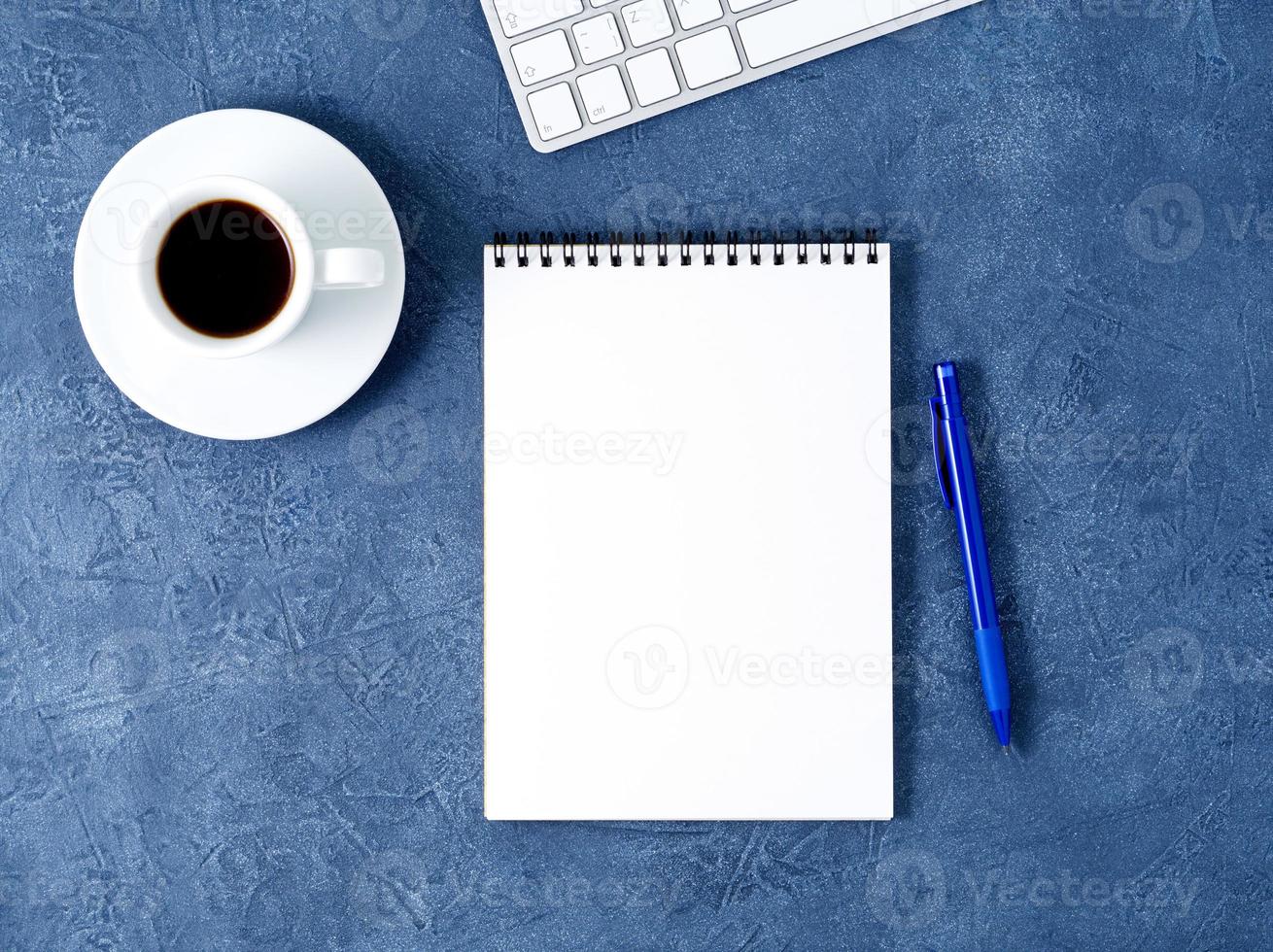 el bloc de notas abierto con una página blanca limpia, un bolígrafo y una taza de café sobre una mesa de piedra azul oscuro envejecida, vista superior foto