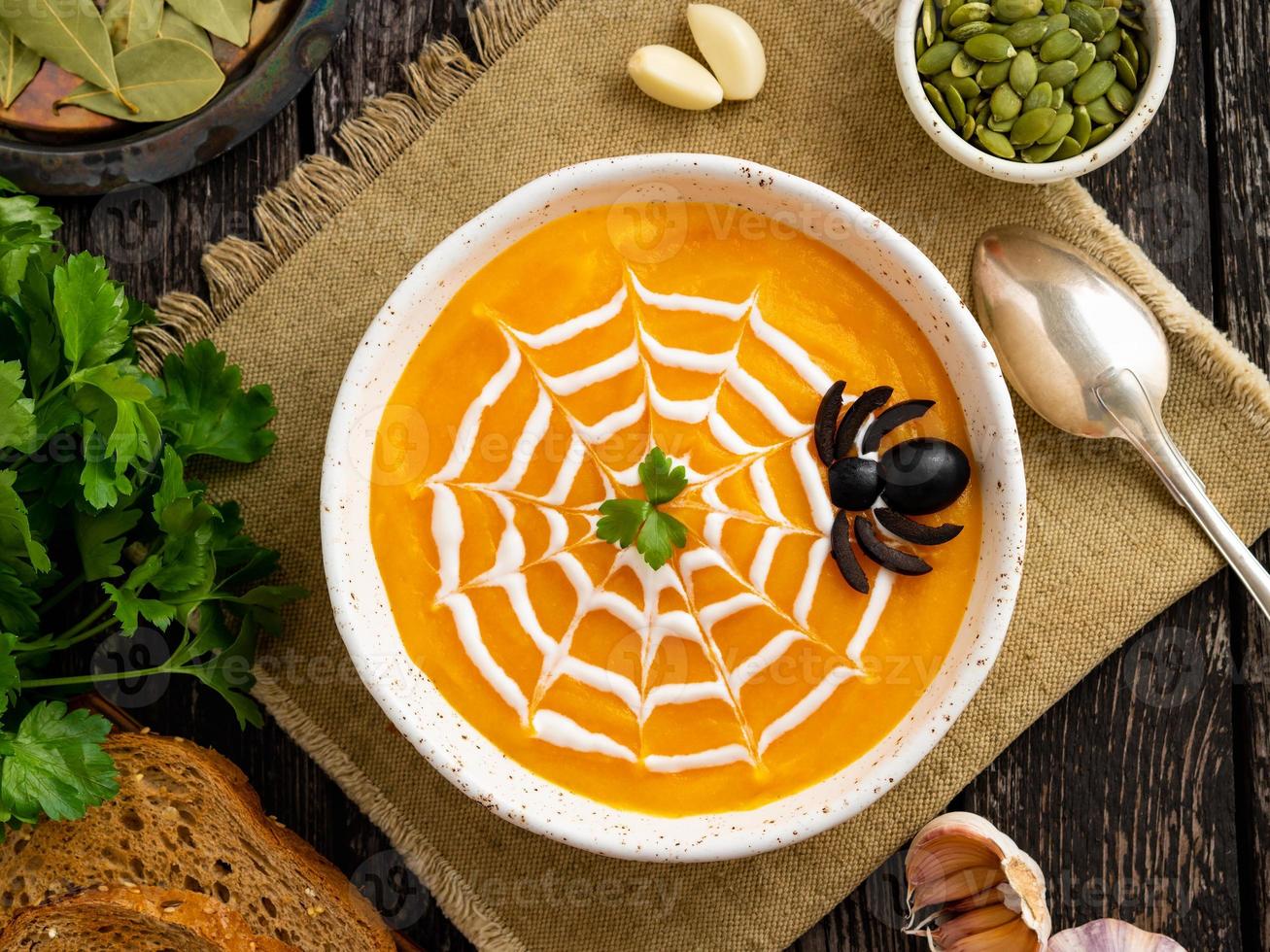 Funny food for Halloween. Pumpkin puree soup, spider web, dark old wooden table, top view. photo