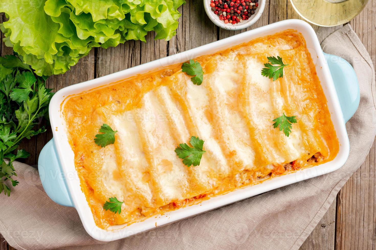 canelones rellenos de carne molida, tomates, horneados con salsa de tomate bechamel, vista superior, fondo antiguo de madera oscura foto