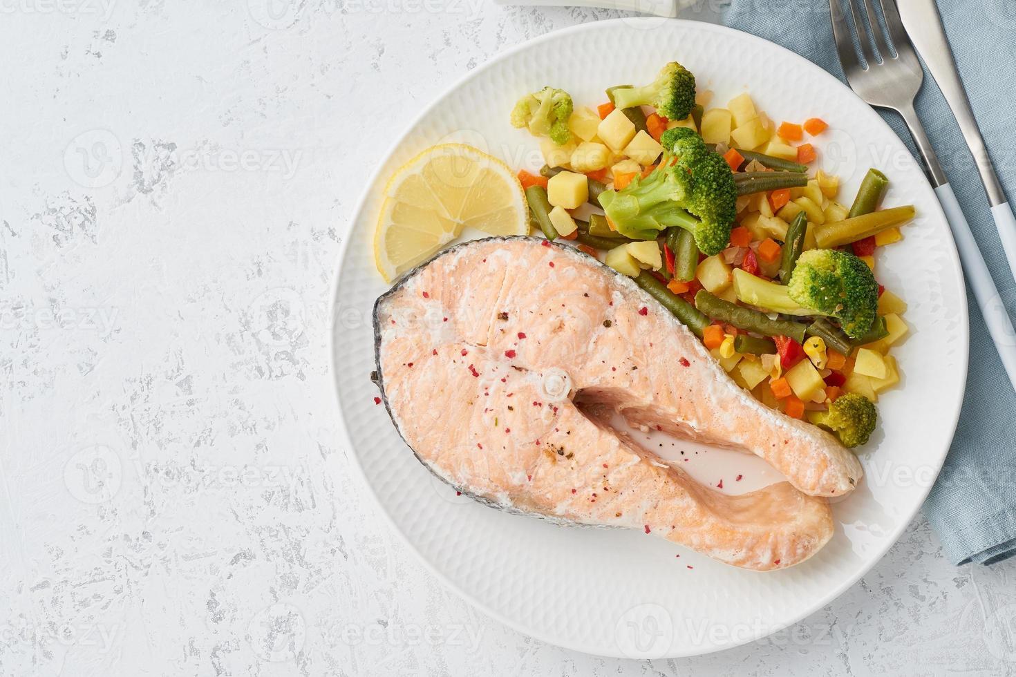 salmón al vapor y verduras, dieta saludable. plato blanco sobre mesa de hormigón, vista superior, espacio de copia foto