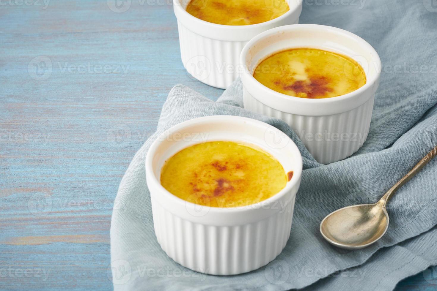 crema catalana, postre español en tres ramekin sobre mesa azul, espacio de copia foto