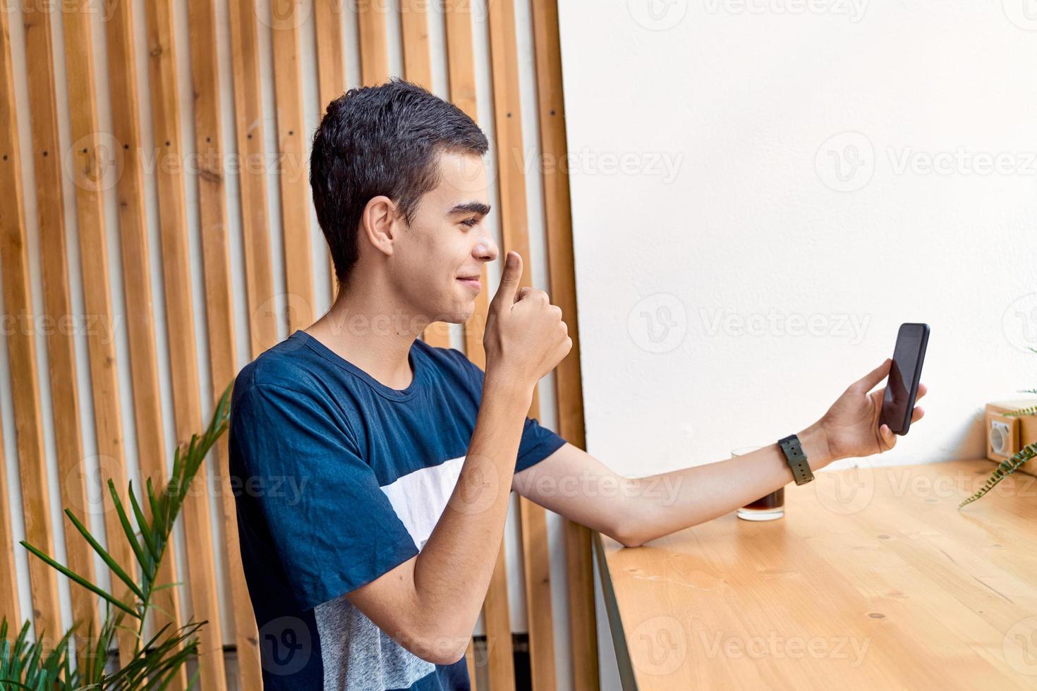 Young adult shows thumb up the phone, smiling. Teenager talking in chat. Blogger communicates online, broadcast photo