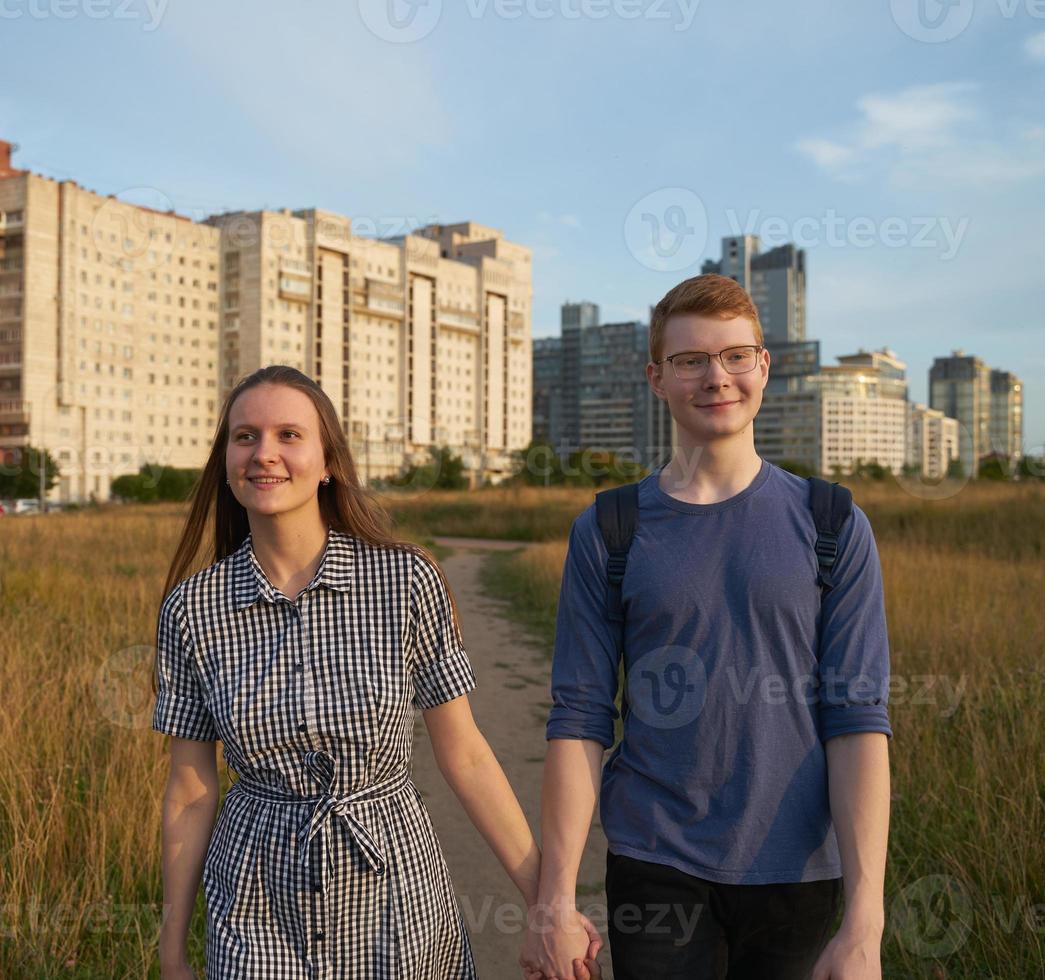 Teen couple walking in field, boy and girl holding hands ans smiling photo