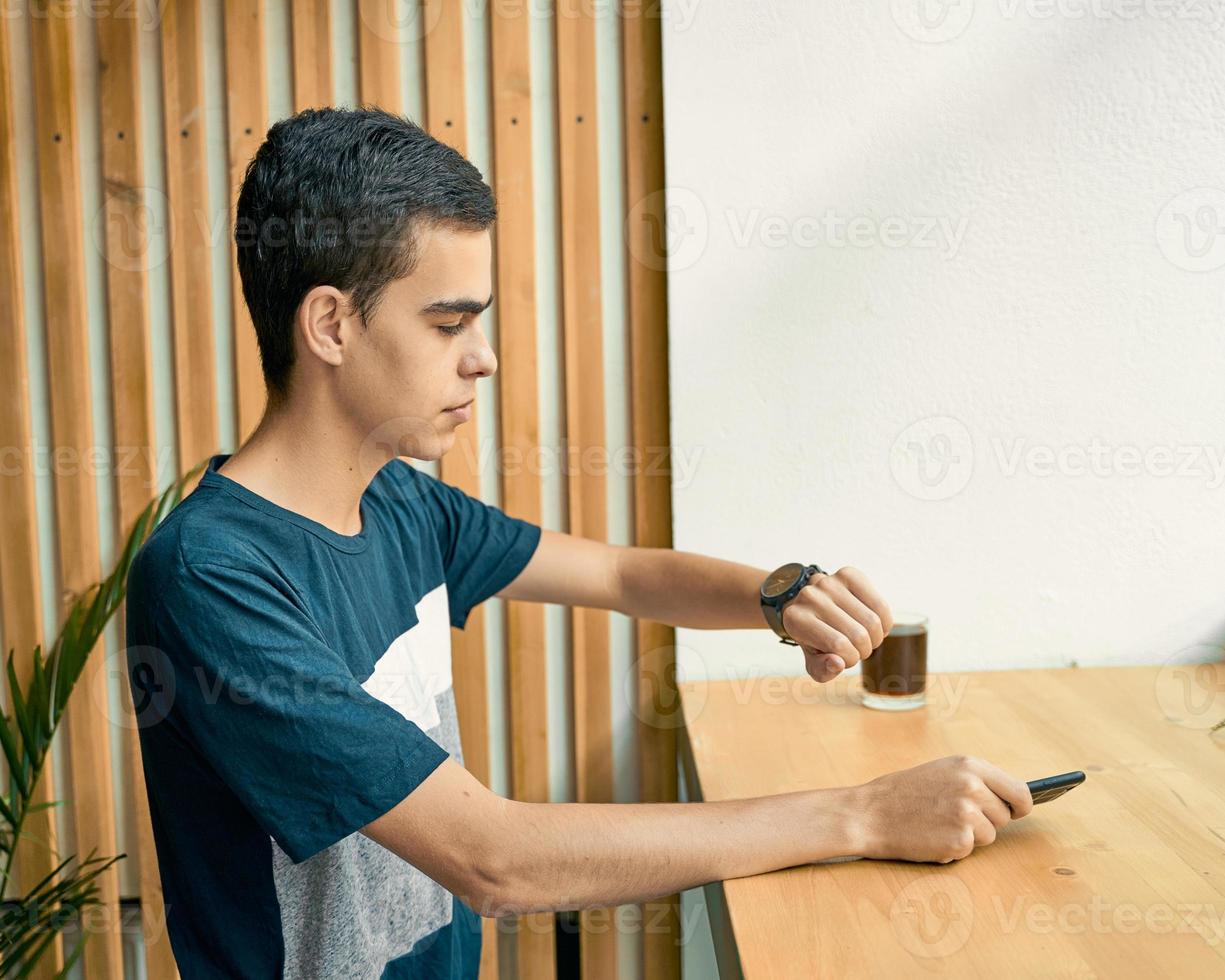 adulto joven mira el reloj, esperando una reunión con amigos. un hombre está esperando a una mujer en un café en una cita, mirando el reloj foto