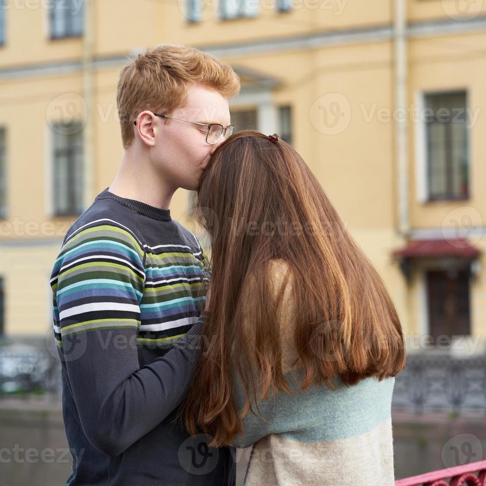 un hombre pelirrojo besa a una mujer en la parte superior de su cabeza, un chico con un suéter calma y consuela a una chica con el pelo largo y oscuro foto