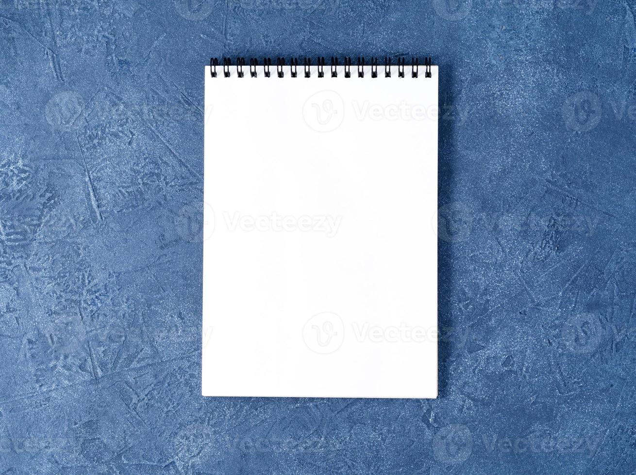 The open notepad with clean white page on aged dark blue stone table, top view photo
