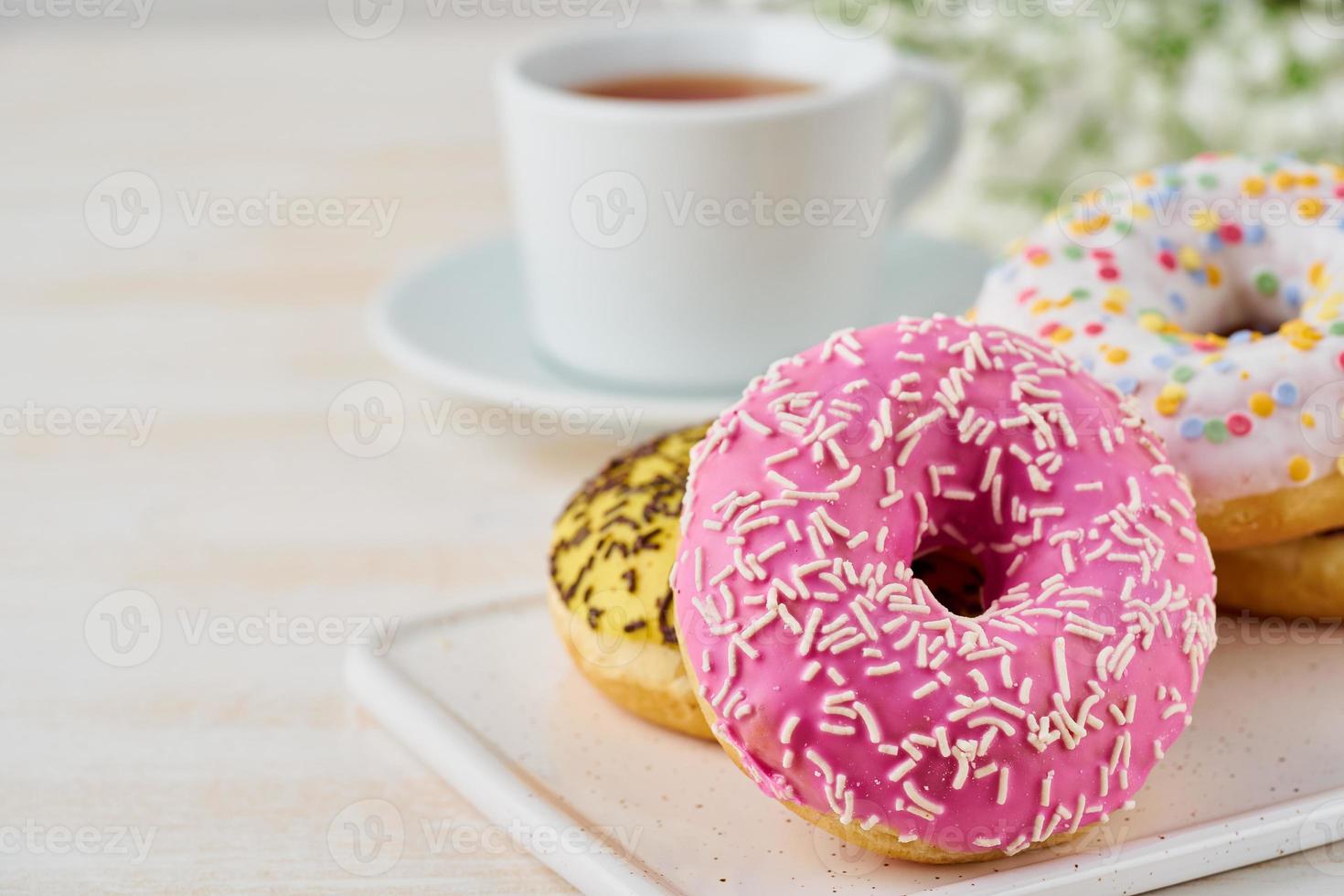 Doughnuts and tea. Bright, colorful junk food. Light beige wooden background. Side view, close up. photo