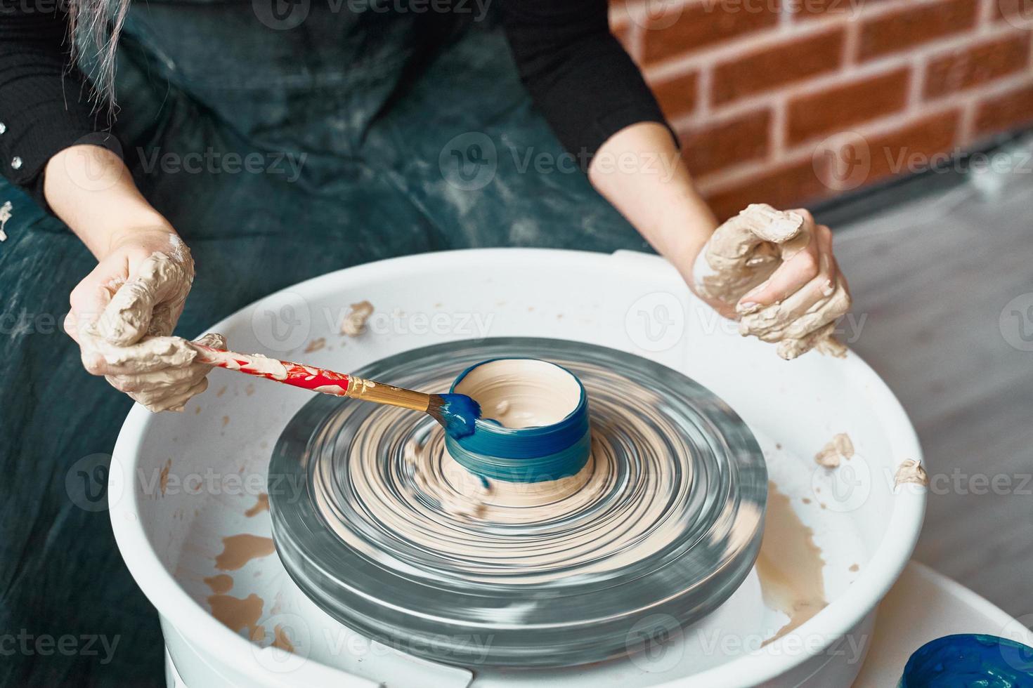 Unrecognisable woman making ceramic pottery on wheel, paints blue. Concept for woman in freelance, business. Handcraft product. Earn extra money, side hustle, turning hobbies into cash photo