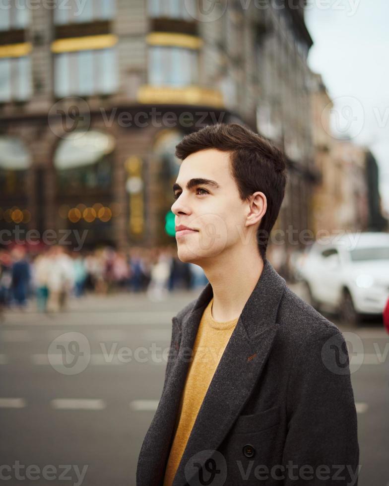 apuesto hombre de moda con estilo, morena con elegante abrigo gris, se encuentra en la calle en el centro histórico de st. petersburgo joven de cabello oscuro, cejas pobladas. foto