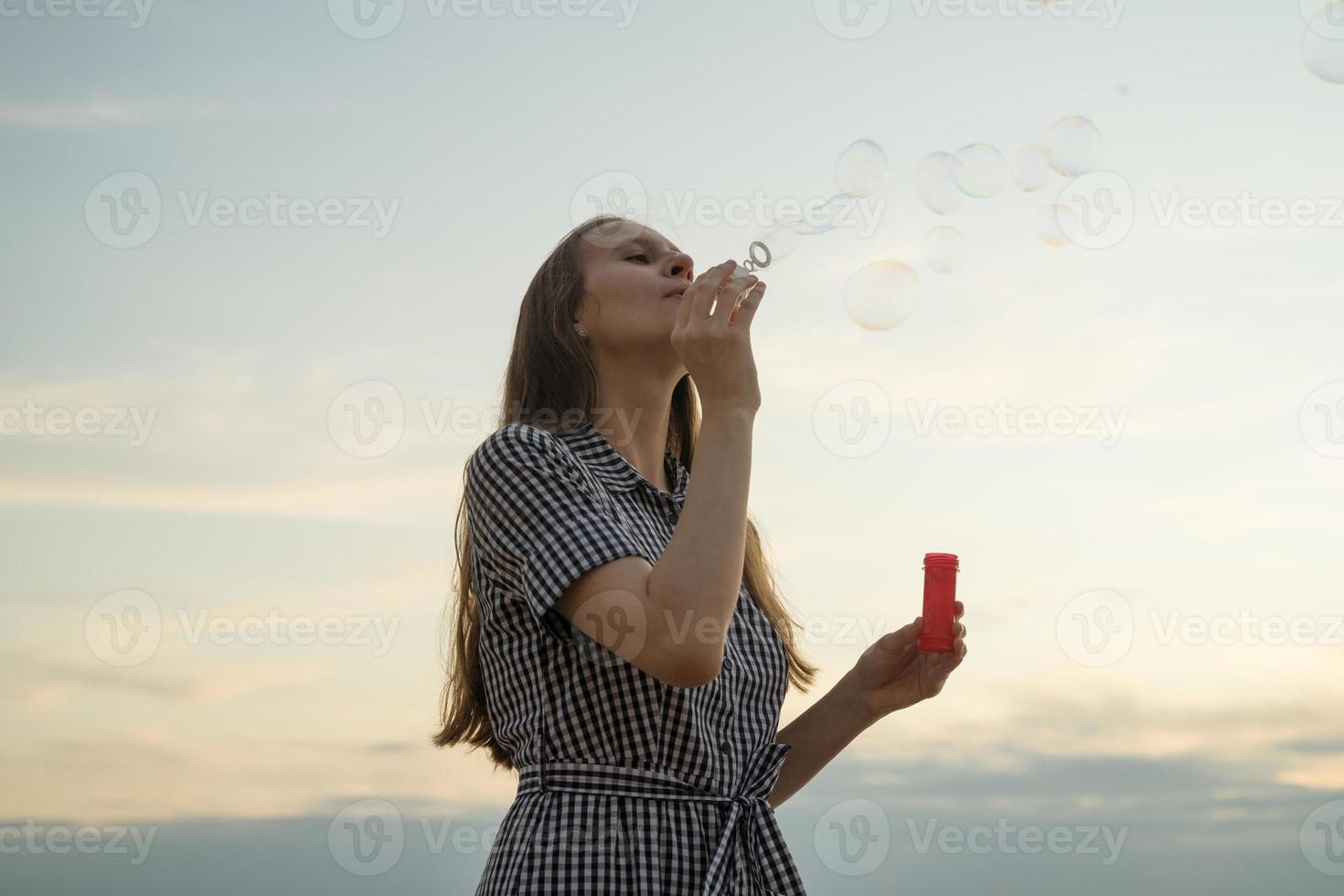 adolescente soplando burbujas de sopa, concepto de diversión y alegría, cielo y nubes en el fondo foto