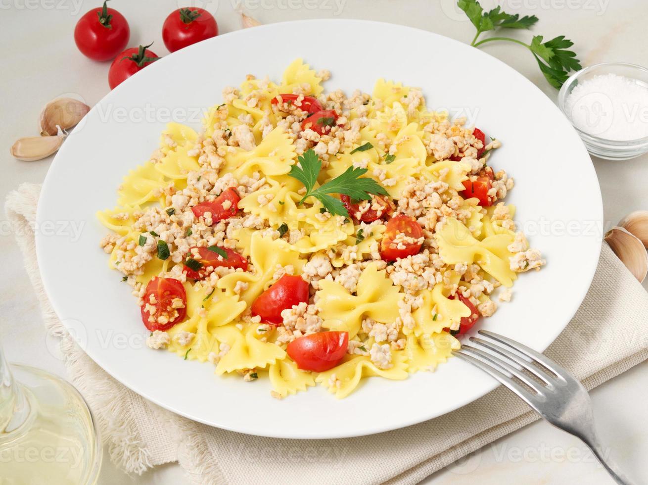 farfalle pasta with tomatoes, chiken meat, parsley on white stone background, low-calorie diet, side view photo