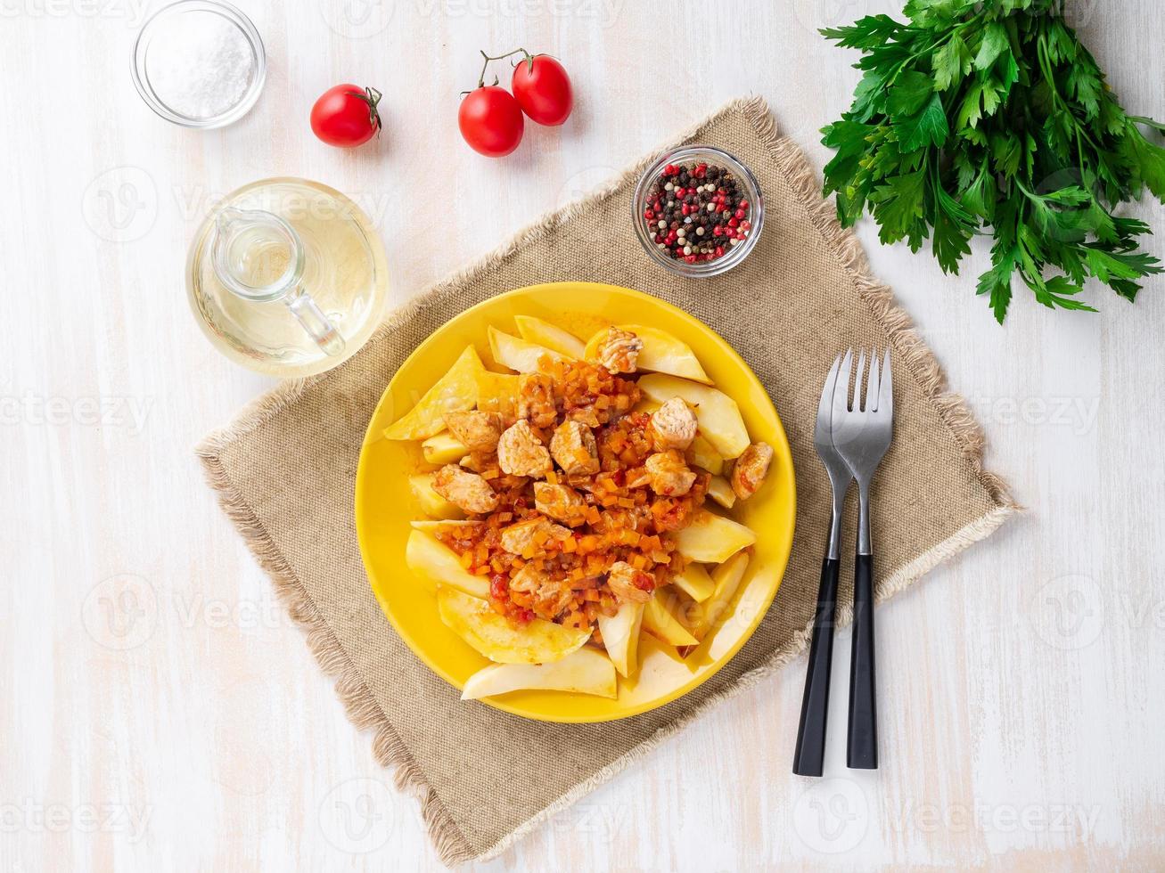 baked potato slices and turkey stew with vegetables on bright yellow plate, on white rustic background, top view, overhead photo