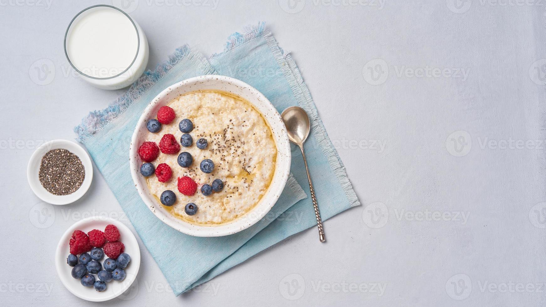 Oatmeal with berries, chia, maple syrup and glass of milk photo