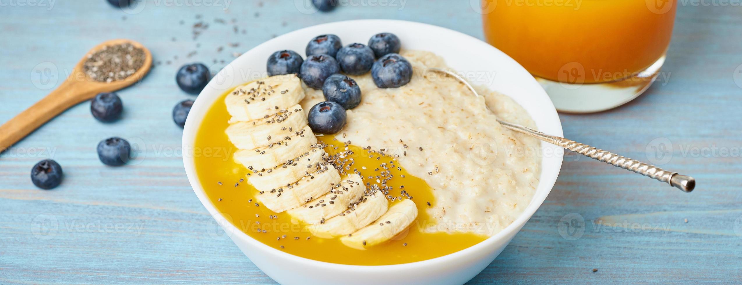 Banner with oatmeal, bananas, blueberries, chia seeds, mango jam on blue wooden background photo