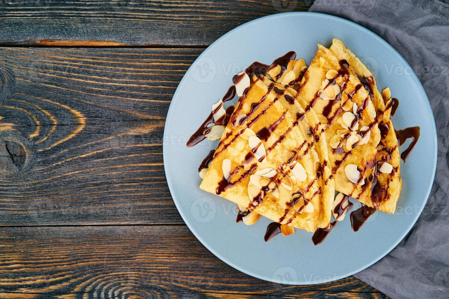 Two pancakes with chocolate syrup, almond flakes on plate, honey flows from spoon photo