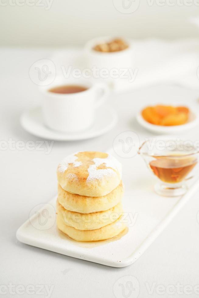 Fried cheese cakes, sweet cheese pancakes on white plate on white background, vertical. Home tea party photo