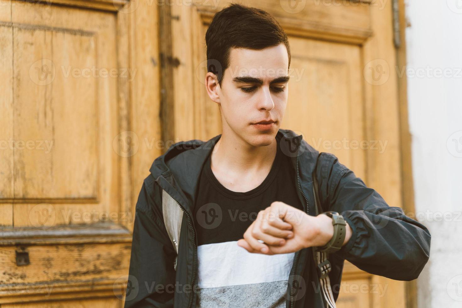 chico adulto joven mira el reloj. tiempo perdido, el concepto de falta de tiempo. hombre caucásico estresado con cabello negro con miedo de llegar tarde. la chica llega tarde a la cita foto