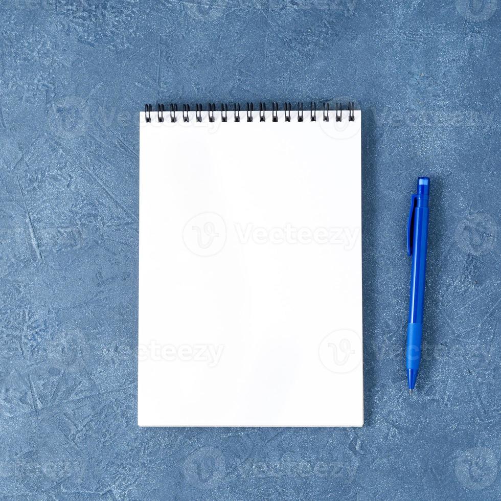 The open notepad with clean white page on aged dark blue stone table, top view photo