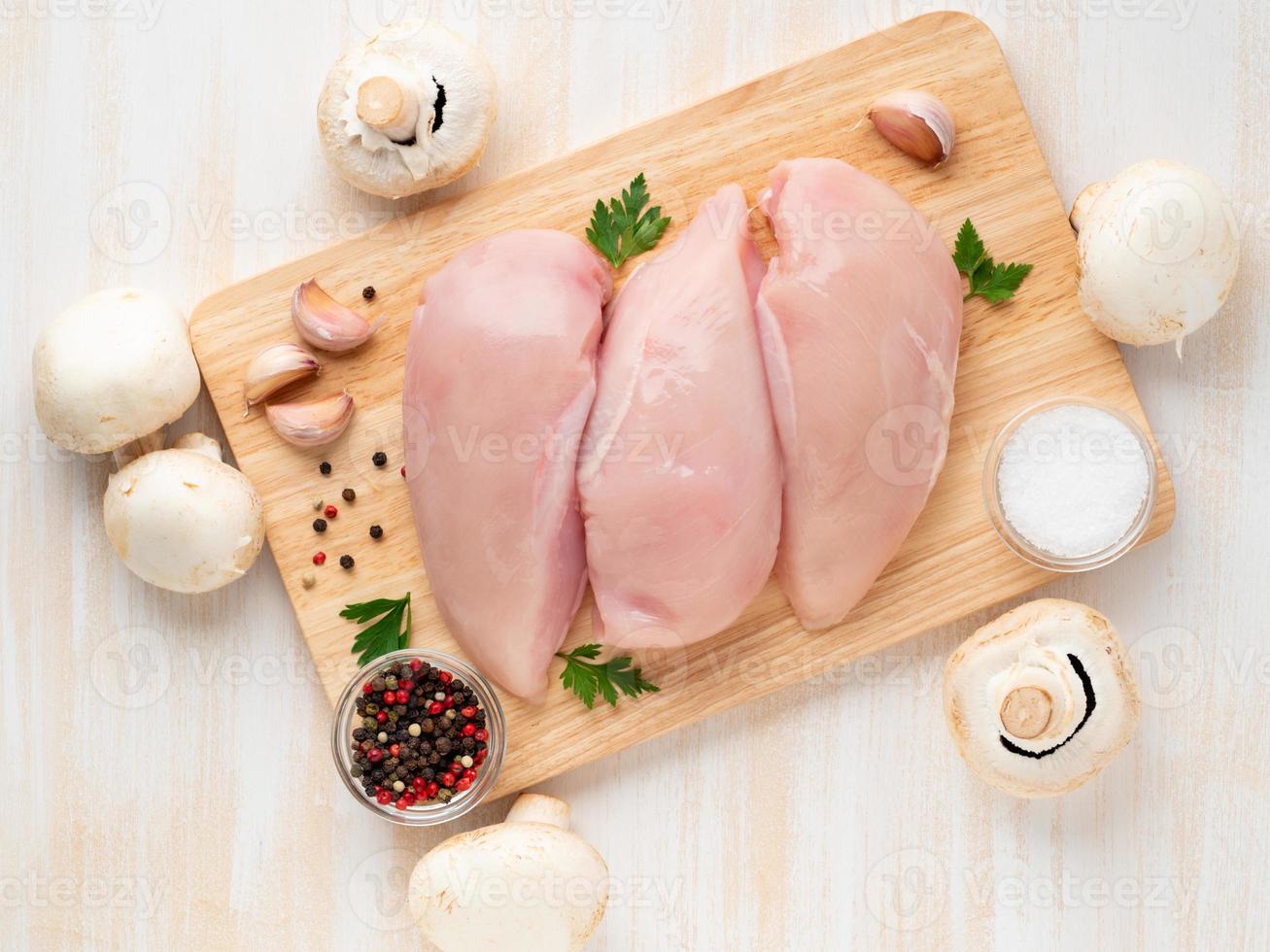 raw chicken breast fillet with spices on wooden board on white wooden table photo