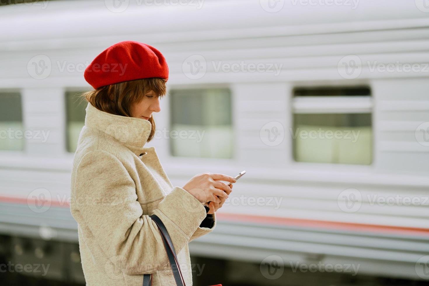 Railway station. Beautiful girl is waiting for train and looks at cell phone. Woman travels light. photo